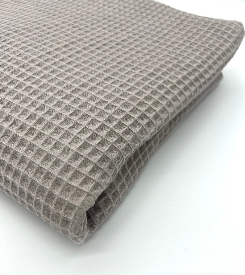May include: A close-up of a folded waffle weave fabric in a light brown color. The fabric has a textured, waffle-like pattern.