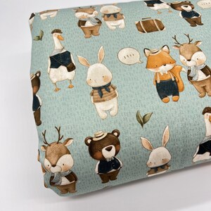May include: A light blue fabric with a repeating pattern of various animals wearing hats and clothing. The animals include a deer, a fox, a rabbit, a goose, and a bear. The fabric has a subtle textured appearance.