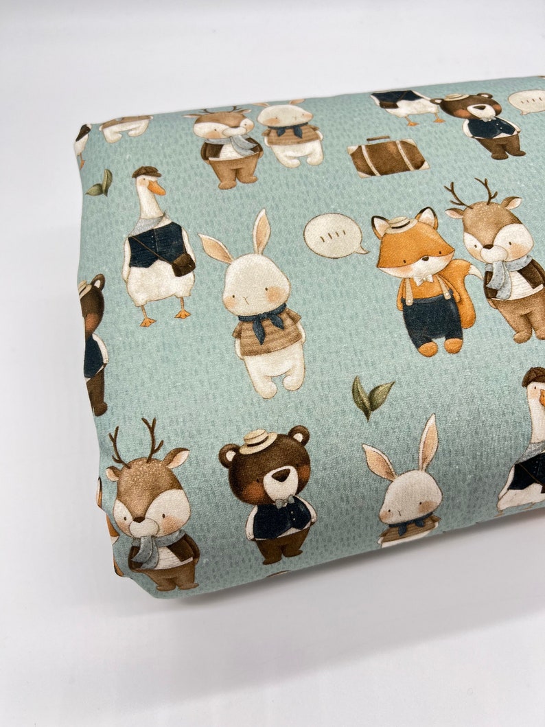 May include: A light blue fabric with a repeating pattern of various animals wearing hats and clothing. The animals include a deer, a fox, a rabbit, a goose, and a bear. The fabric has a subtle textured appearance.