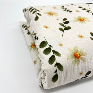 Può includere: Un tessuto bianco con un motivo floreale di foglie verdi e fiori gialli. Il tessuto è piegato a metà e il motivo è visibile su entrambi i lati.