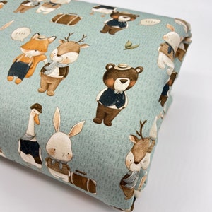 May include: A light blue fabric with a repeating pattern of various animals wearing hats and carrying suitcases. The animals include a fox, a deer, a bear, a rabbit, and a goose. The fabric has a subtle texture.