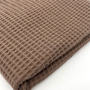 May include: A brown waffle weave fabric folded in half. The fabric has a textured, waffle-like pattern.