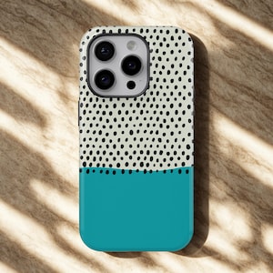 以下が含まれることがあります： ツートンカラーのデザインのスマートフォンケース。上半分は、黒い点が散りばめられたクリーム色の背景で、下半分は無地のターコイズ色です。ケースにはカメラの切り抜きがあり、耐久性のあるプラスチック製である可能性があります。