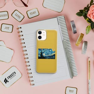 May include: A mustard yellow smartphone case featuring a rectangular print of Vincent van Gogh's The Starry Night painting. The case has a dual-camera cutout at the top left and is positioned on a spiral-bound notebook with lined pages.