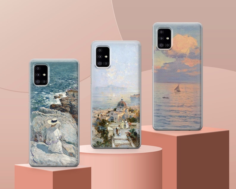 May include: Three different phone cases with scenic images. The first case features a seascape with a woman in a hat standing on a rocky cliff. The second case shows a cityscape with a church and buildings. The third case has a seascape with a sailboat in the distance.
