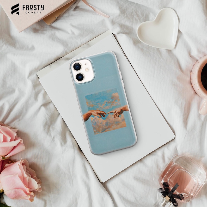 May include: A light blue smartphone case featuring a central square graphic of the Creation of Adam painting, showing two hands reaching toward each other against a backdrop of soft, orange-toned clouds and a light blue sky.