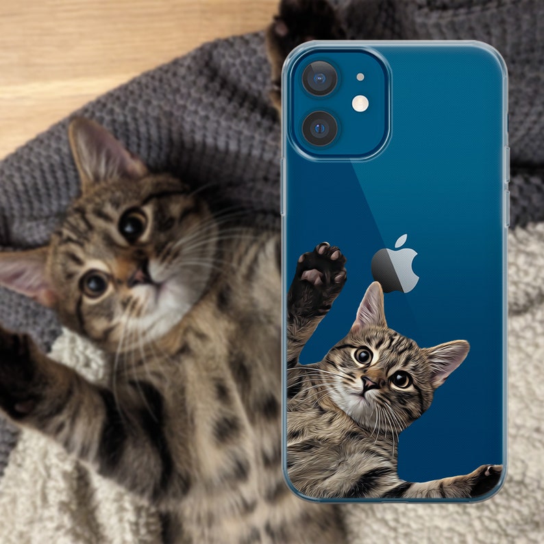 Pu&ograve; includere: Custodia trasparente per telefono con un design a gatto tigrato. L'illustrazione del gatto si estende verso un logo Apple su sfondo blu. Un vero gatto tigrato &egrave; sullo sfondo.