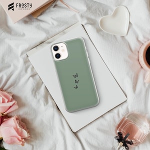 K&ouml;nnte beinhalten: Eine salbeigr&uuml;ne Handyh&uuml;lle mit minimalistischem Design, das drei schwarze Schmetterlings-Silhouetten zeigt. Die H&uuml;lle ist f&uuml;r ein Smartphone mit Kamerabuckel konzipiert.