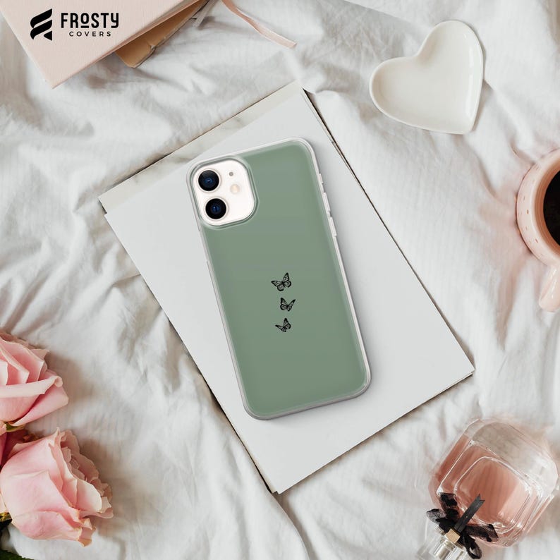 K&ouml;nnte beinhalten: Eine salbeigr&uuml;ne Handyh&uuml;lle mit minimalistischem Design, das drei schwarze Schmetterlings-Silhouetten zeigt. Die H&uuml;lle ist f&uuml;r ein Smartphone mit Kamerabuckel konzipiert.