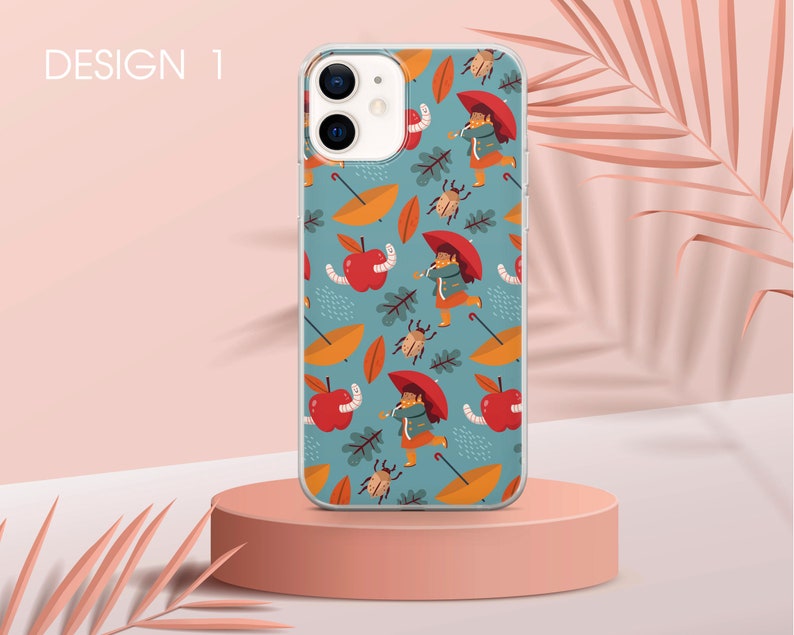 May include: A clear phone case featuring a colourful pattern of red apples, green leaves, brown beetles, yellow umbrellas, and a girl wearing a red hat and blue jacket. The pattern is repeated on a blue background.