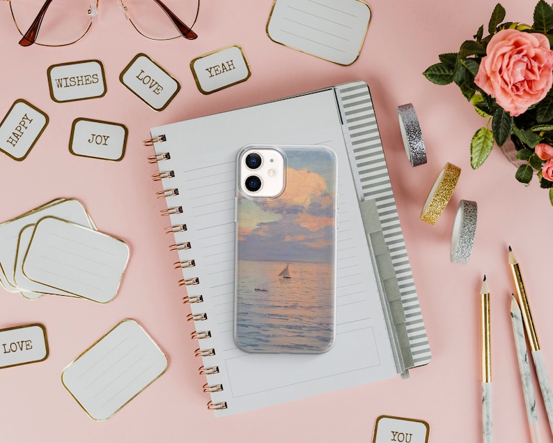 May include: A clear phone case with a sunset and sailboat image on a pink background with a notebook, pencils, and decorative tape.