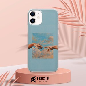 May include: A light blue smartphone case featuring a rectangular print of two hands reaching toward each other against a backdrop of clouds. The case has a clear border and a cutout for a dual-lens camera system on the upper left corner.