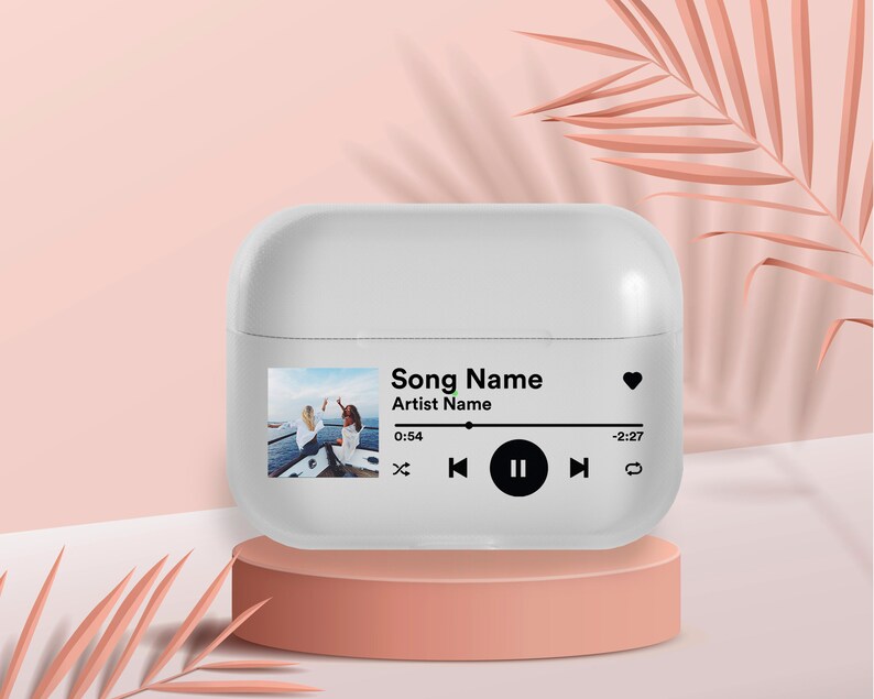May include: White Airpods case with a custom design featuring a photo of two people on a boat, the text "Song Name", "Artist Name", and a music player control bar with play, pause, and skip buttons.