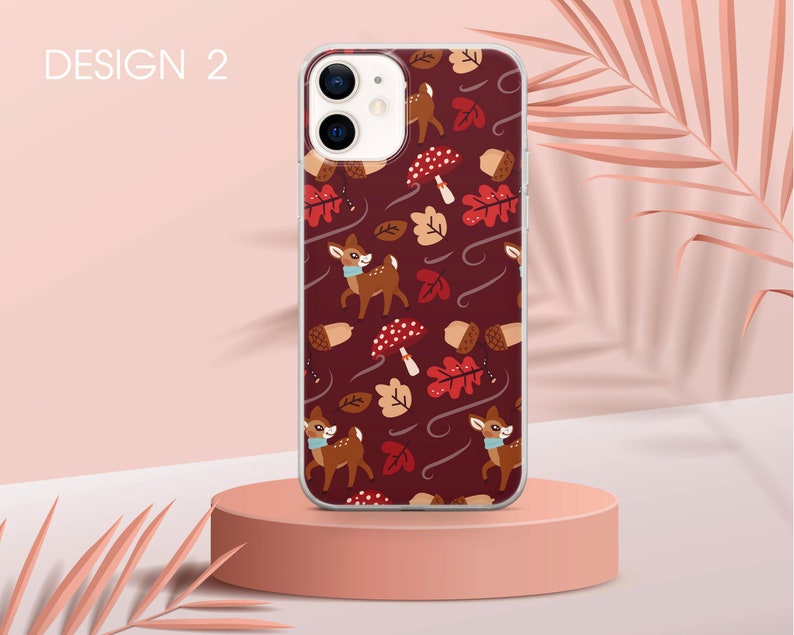 May include: A phone case with a red background and a pattern of deer, mushrooms, and leaves. The case is clear and shows the phone's camera lens.