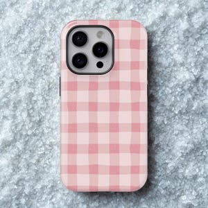 Könnte beinhalten: Eine Handyhülle mit rosa und weißem Vichy-Muster. Die Hülle hat einen schwarzen Kamerarand und eine glatte, glänzende Oberfläche. Das Design zeigt ein klassisches, handgemaltes Karomuster.