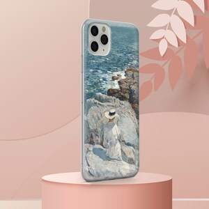 May include: A clear phone case with a painting of a woman in a white dress and a straw hat sitting on a rocky cliff overlooking a blue ocean. The phone case has a camera cutout and a white background.
