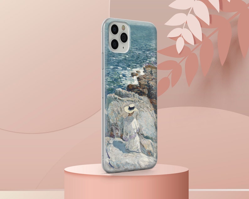 May include: A clear phone case with a painting of a woman in a white dress and a straw hat sitting on a rocky cliff overlooking a blue ocean. The phone case has a camera cutout and a white background.