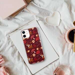 May include: A clear phone case with a red, white and brown autumn-themed design. The design features small deer, leaves and acorns.