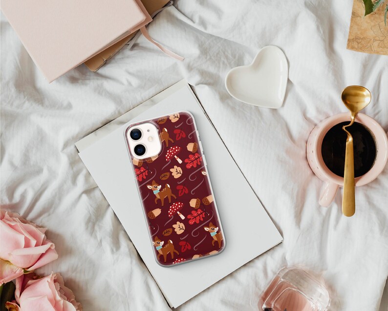 May include: A clear phone case with a red, white and brown autumn-themed design. The design features small deer, leaves and acorns.
