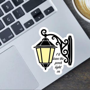 May include: A black and yellow sticker featuring a stylized porch light with the text "I'll leave the porch light on." The sticker is on a laptop, with a keyboard visible in the background.