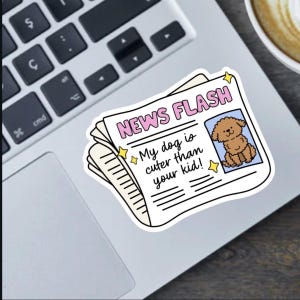 Peut inclure: Un autocollant avec un design de journal, avec le titre "NEWS FLASH" en rose. Le texte "My dog is cuter than your kid!" est affiché, avec une illustration de caniche. L'autocollant est sur un ordinateur portable.