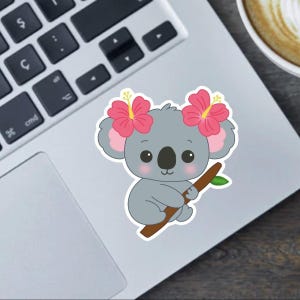 Pode incluir: Um autocolante com um coala de desenho animado com pelo cinzento, orelhas cor-de-rosa e olhos grandes e pretos. O coala usa duas flores de hibisco cor-de-rosa e segura um ramo castanho com uma folha verde. O autocolante está colocado num portátil.