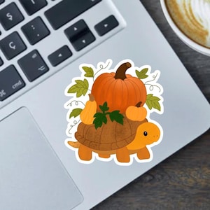May include: A colorful sticker featuring a cartoon turtle carrying pumpkins and leaves. The turtle is orange and brown, with a friendly expression. The pumpkins are various sizes and shades of orange. The sticker is placed on a laptop.
