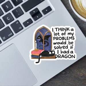 Pode incluir: Um autocolante com uma ilustração fantástica. Mostra um gato preto, um dragão, uma vela e livros em frente a uma janela. O texto diz: "I THINK a lot of my PROBLEMS would be solved if I had a DRAGON."