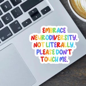 May include: A colorful sticker with the text "EMBRACE NEURODIVERSITY. NOT LITERALLY. PLEASE DON'T TOUCH ME." The text is in rainbow colors and is on a white background. The sticker is on a laptop.