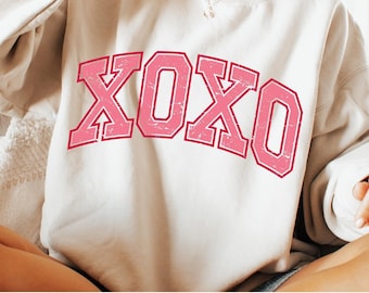 May include: A white sweatshirt with a pink "XOXO" graphic in a vintage collegiate style font.