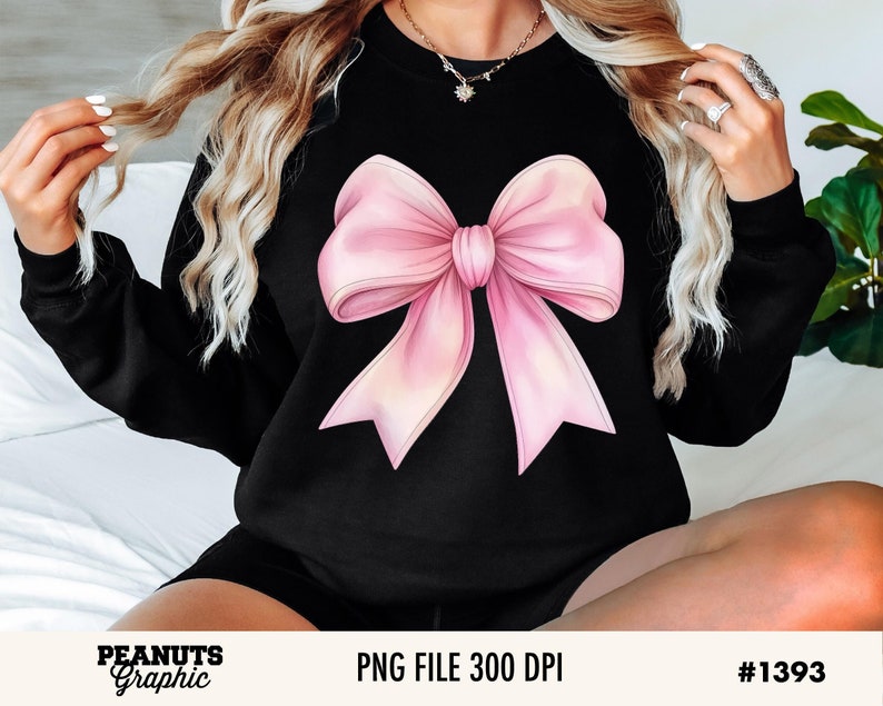 May include: A black sweatshirt with a large pink bow graphic on the front. The bow is a light pink color with a darker pink center.