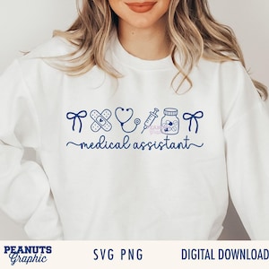 May include: A white long-sleeve sweatshirt featuring a dark blue graphic print. The design includes icons of two bows, a bandage, a stethoscope, a syringe, and a pill bottle, with the text medical assistant written in a cursive script font.