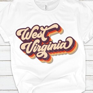 K&ouml;nnte beinhalten: Wei&szlig;es T-Shirt mit einer Retro-Grafik, auf der "West Virginia" in einer mehrfarbigen Schrift steht.