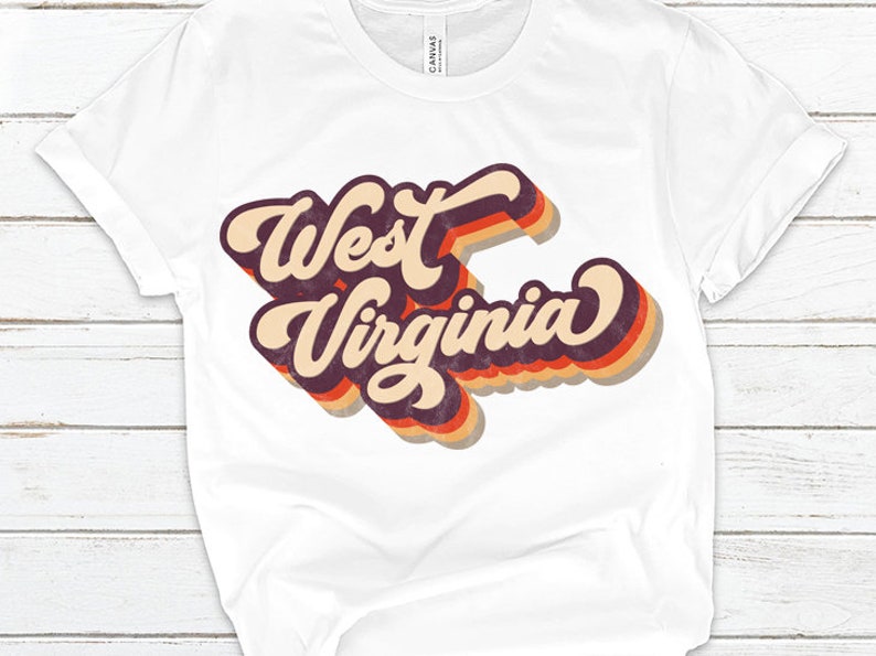 K&ouml;nnte beinhalten: Wei&szlig;es T-Shirt mit einer Retro-Grafik, auf der "West Virginia" in einer mehrfarbigen Schrift steht.