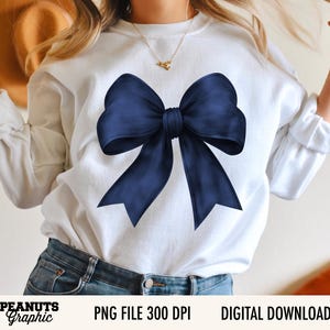 Op de afbeelding: Witte sweatshirt met een grote, marineblauwe strik. De strik staat centraal op de voorkant van de trui. De tekst "PEANUTS Graphic" staat linksonder, met "PNG FILE 300 DPI" en "DIGITAL DOWNLOAD" rechts.