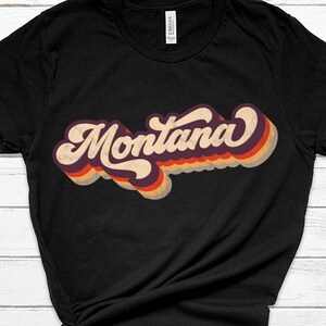 Pu&ograve; includere: Maglietta nera con una grafica in stile retr&ograve; della parola "Montana" in colori arcobaleno.