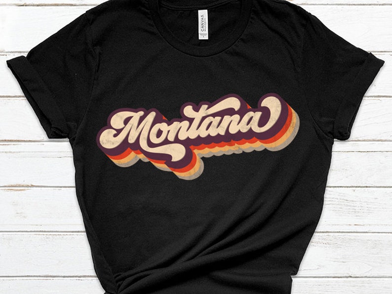 Pu&ograve; includere: Maglietta nera con una grafica in stile retr&ograve; della parola "Montana" in colori arcobaleno.