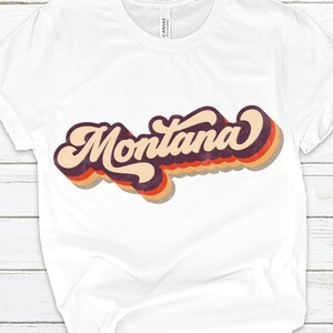 Pu&ograve; includere: Maglietta bianca con una grafica in stile retr&ograve; della parola "Montana" in arancione, rosso e viola.