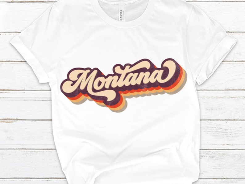 Pu&ograve; includere: Maglietta bianca con una grafica in stile retr&ograve; della parola "Montana" in arancione, rosso e viola.