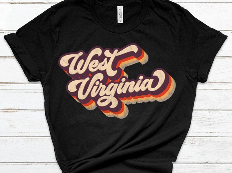 K&ouml;nnte beinhalten: Schwarzes T-Shirt mit einer Retro-Grafik, die "West Virginia" in bunten, &uuml;bereinanderliegenden Buchstaben zeigt.