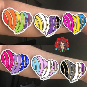 May include: Six heart-shaped stickers with a colorful, layered design resembling a traditional Mexican pastry. Each sticker features a different color combination, including rainbow, yellow, purple, pink, blue, and black.