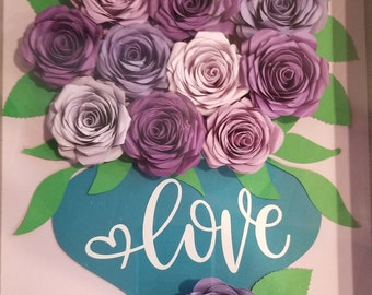 May include: A framed paper craft featuring a bouquet of purple and pink paper roses in a teal vase with the word "love" written in white.
