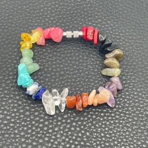 May include: A rainbow chakra bracelet made with natural stones. The bracelet features a variety of colors, including red, orange, yellow, green, blue, indigo, and violet. The bracelet is made with a stretchy cord and has a silver clasp.