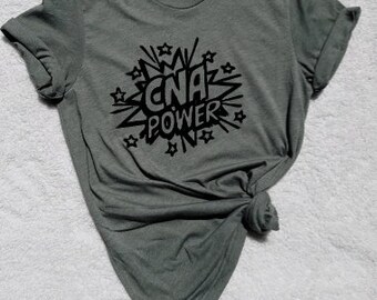May include: A dark green t-shirt with a black graphic print of a comic book style speech bubble that says "CNA POWER".