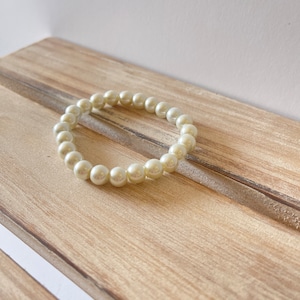 May include: A simple white pearl bracelet with a classic design. The bracelet is made of small, round pearls that are strung together on a clear elastic cord.