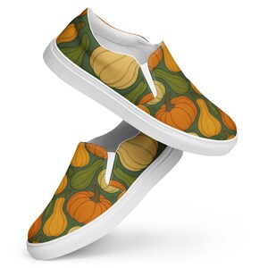 Peut inclure: Paire de chaussures à enfiler avec un motif répété de citrouilles et de courges orange, jaunes et vertes sur fond vert foncé. Les chaussures ont des semelles blanches et des panneaux élastiques blancs.
