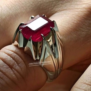 Op de afbeelding: Een zilveren ring met een grote, dieprode, smaragd geslepen edelsteen. De ring heeft een getextureerd, geometrisch ontwerp.