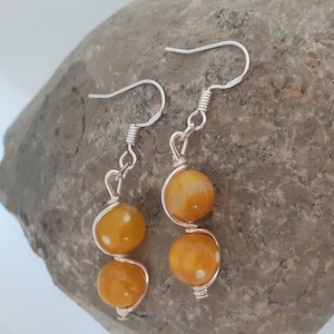 May include: A pair of silver dangle earrings with two yellow and white speckled beads on each earring.