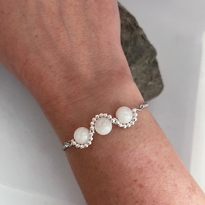 May include: A silver bracelet featuring three white moonstone beads. The beads are arranged in a wave design.