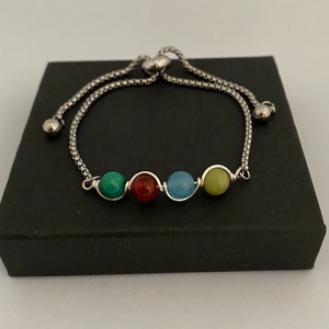 May include: A silver chain bracelet with a sliding clasp and four round gemstone beads in shades of green, red, blue, and yellow.